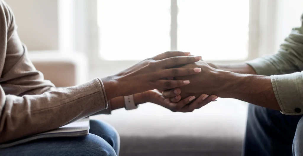 A therapist holding a patient's hands in a supportive gesture during a counseling session on addiction recovery.